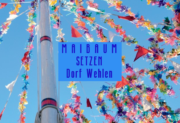 Ausschnitt einer geschmückten Maibaumstange mit bunten Bändern und Wimpeln vor blauem Himmel. Auf einem blauen Rechteck in der Mitte steht in blauer Schrift: Maibaum setzen Dorf Wehlen